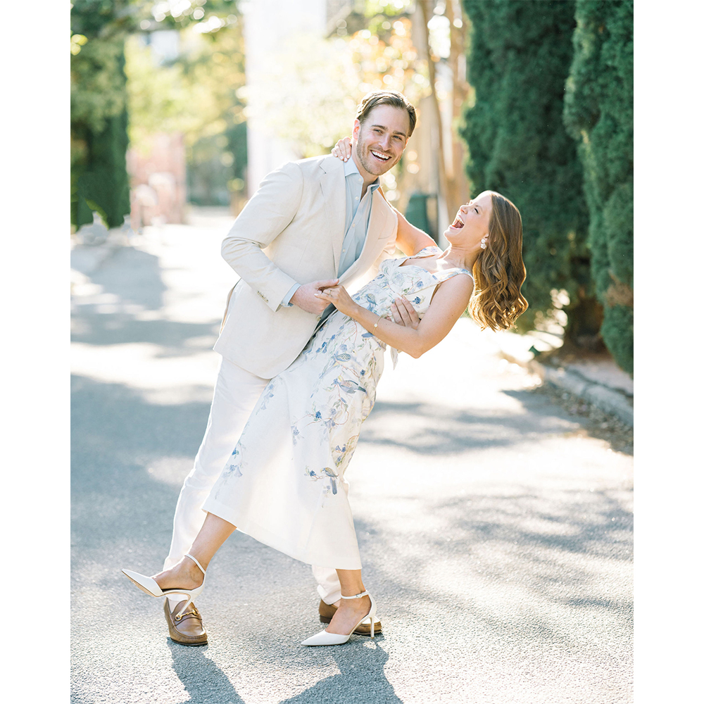 Newlyweds laughing during a playful portrait on a garden drive